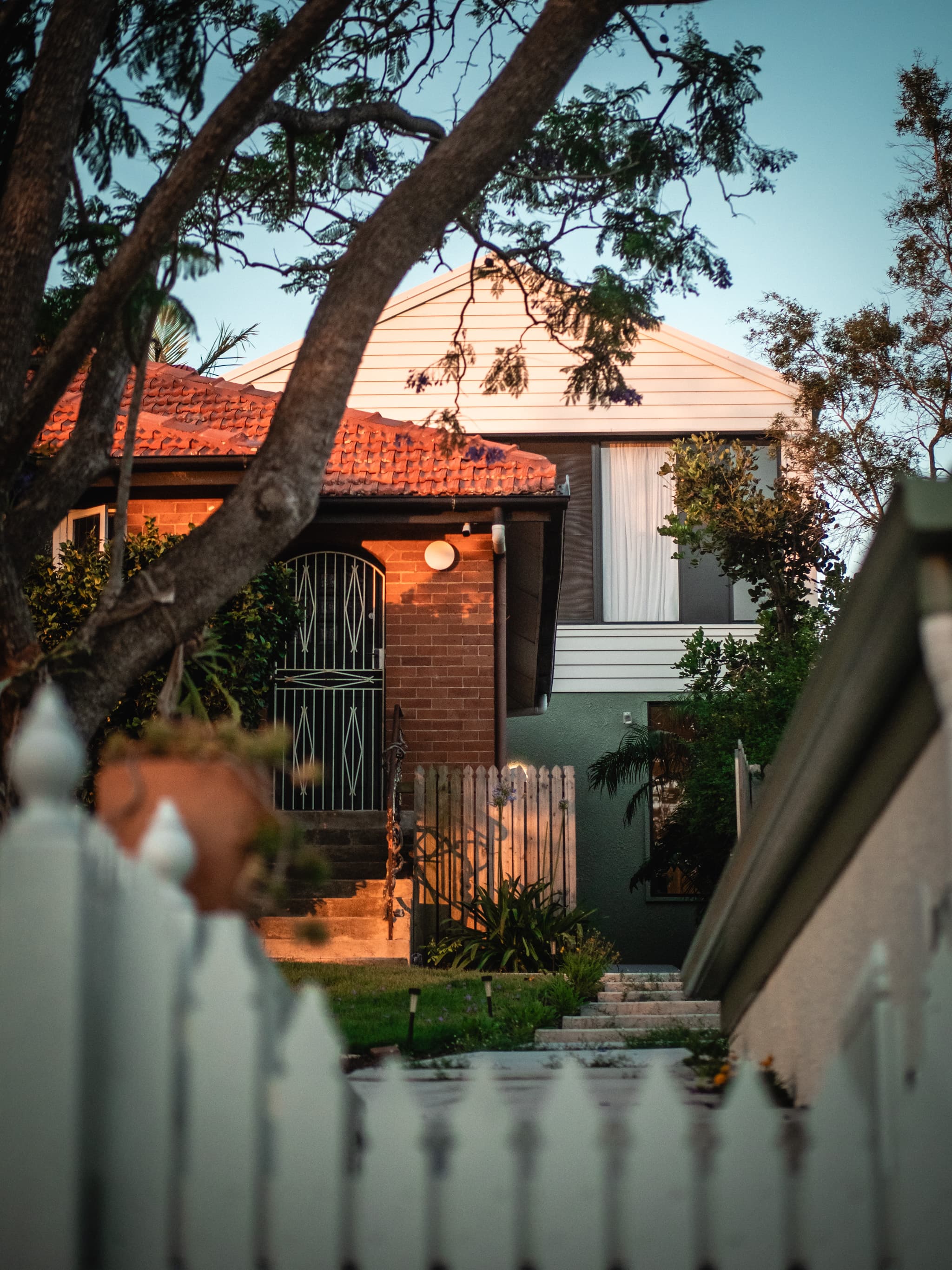 Jacaranda Highside street frontage at dusk, the original brick cottage and tiled roof in front of the new weatherboard upper storey
