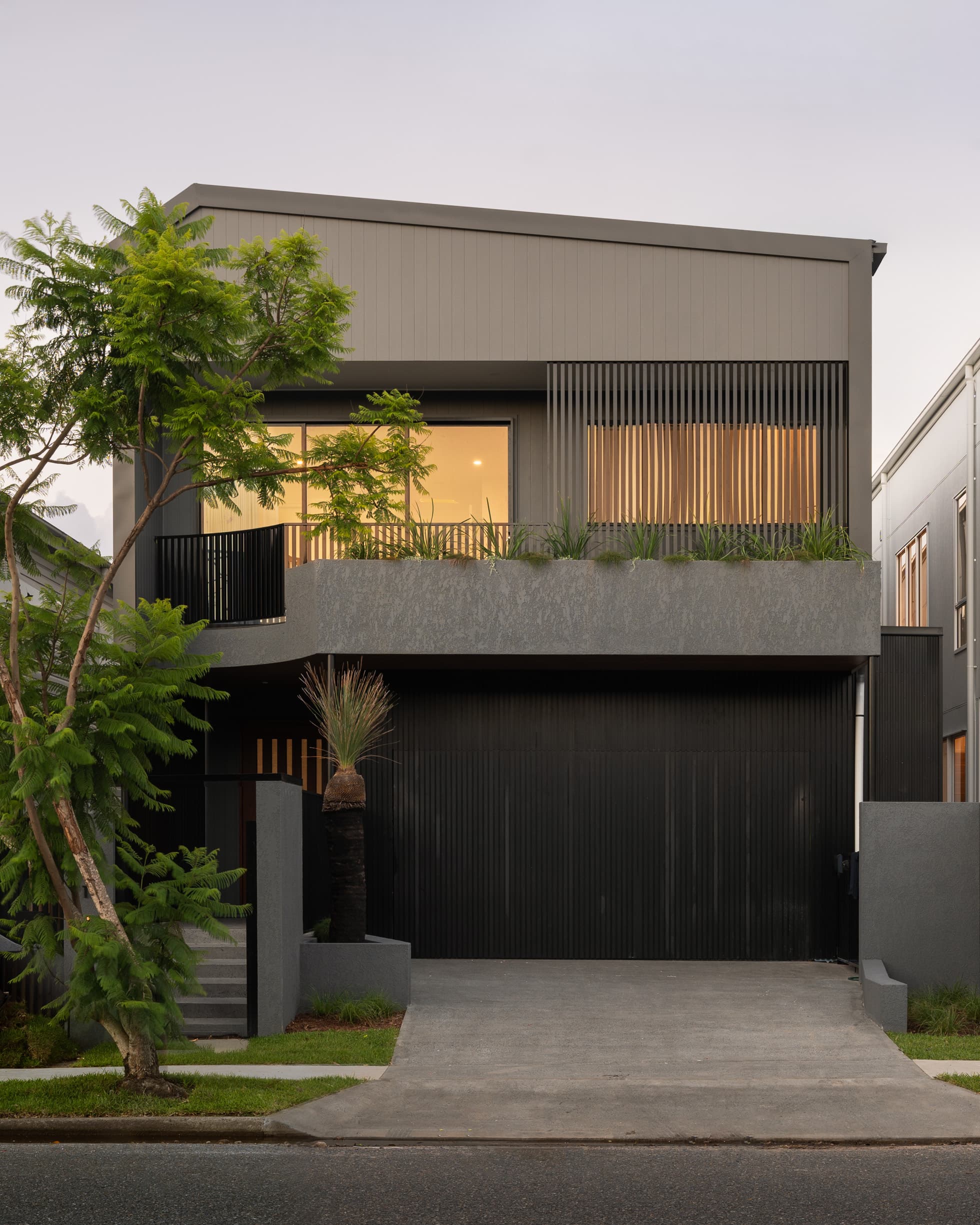 Lindsay House street elevation at dusk with dark vertical cladding and a planted concrete balcony