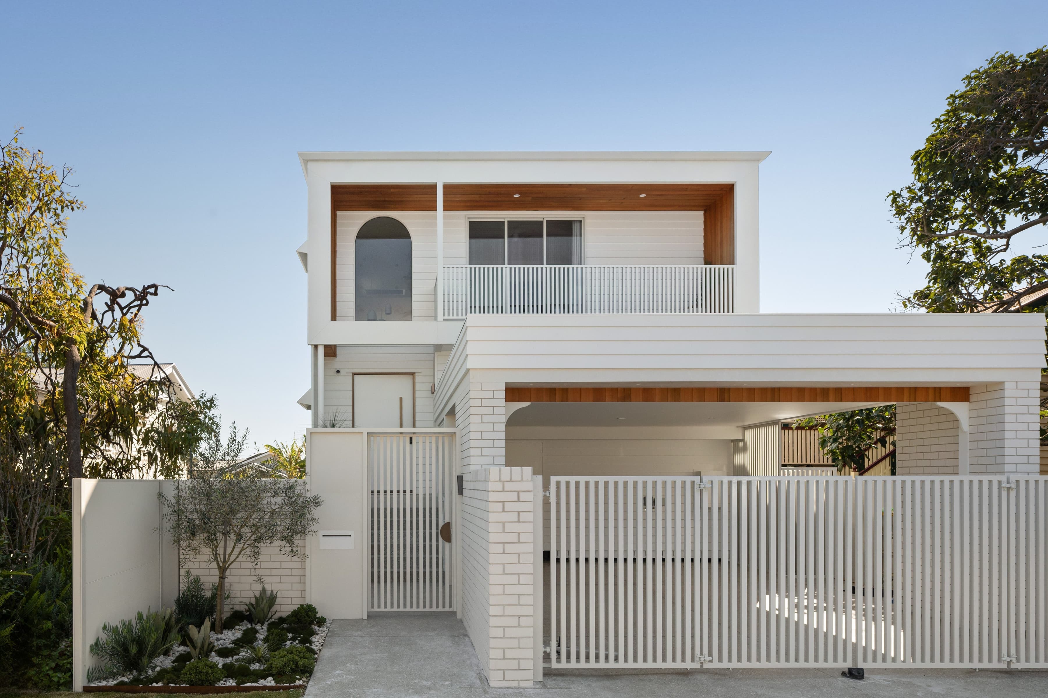 Mesa street elevation in white brick and weatherboard, with a timber-lined balcony soffit above the carport and a white batten fence