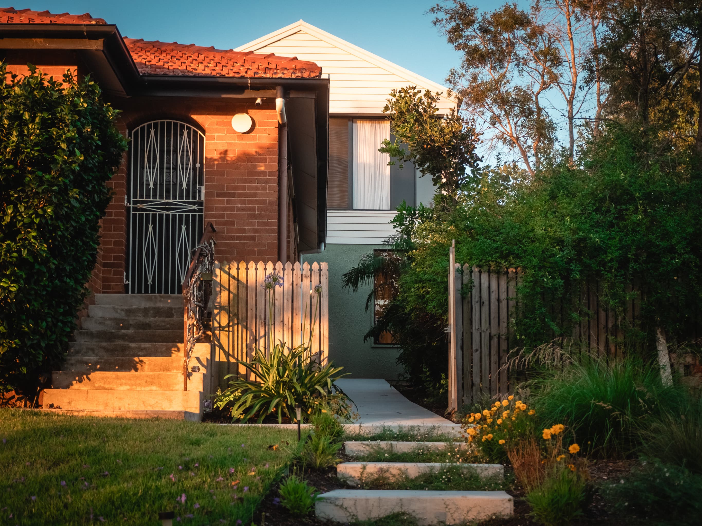 Jacaranda Highside front entry at dusk, brick cottage with an arched screen door and garden path