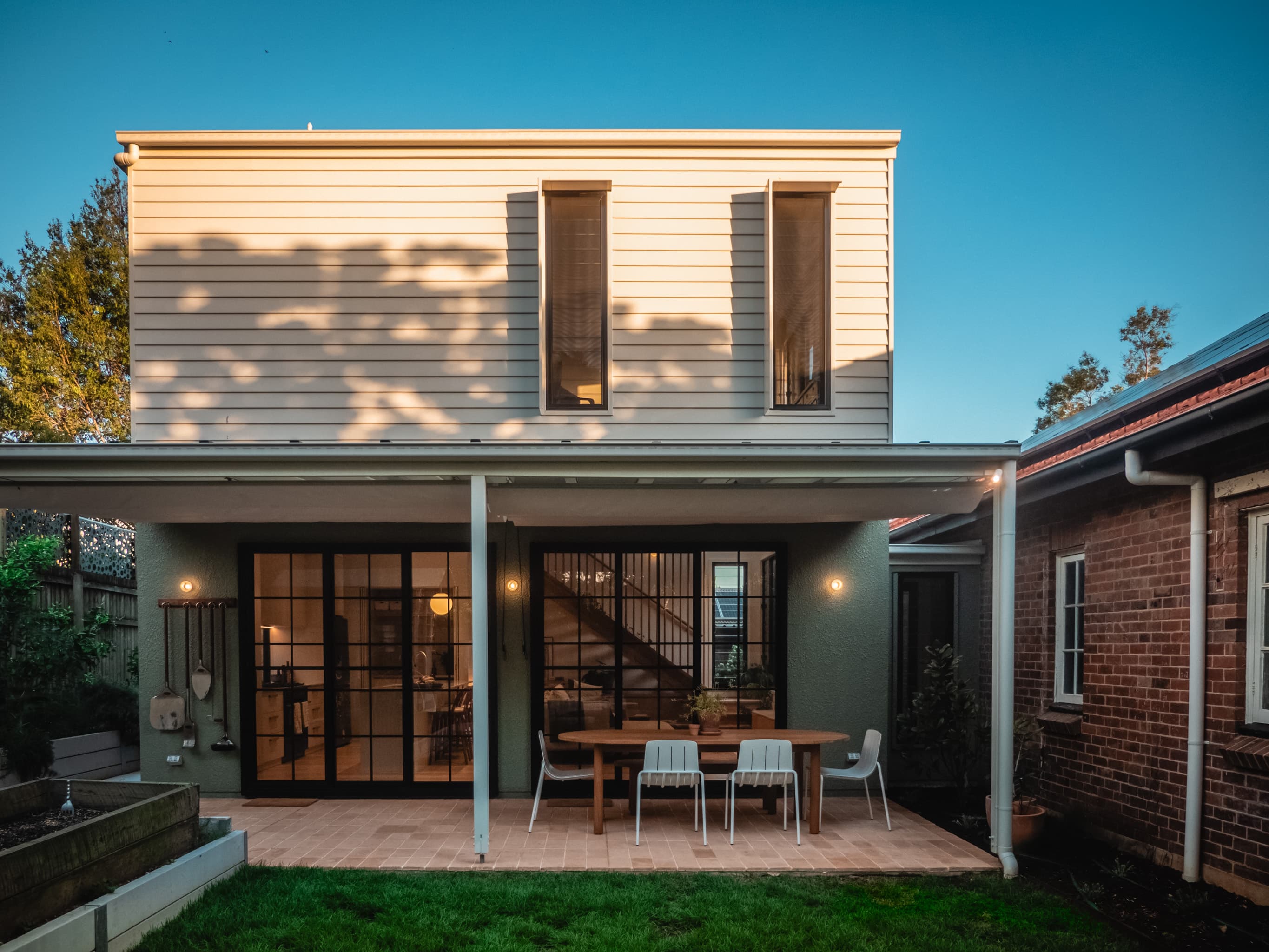 Jacaranda Highside rear elevation at dusk, weatherboard upper storey above a covered dining terrace
