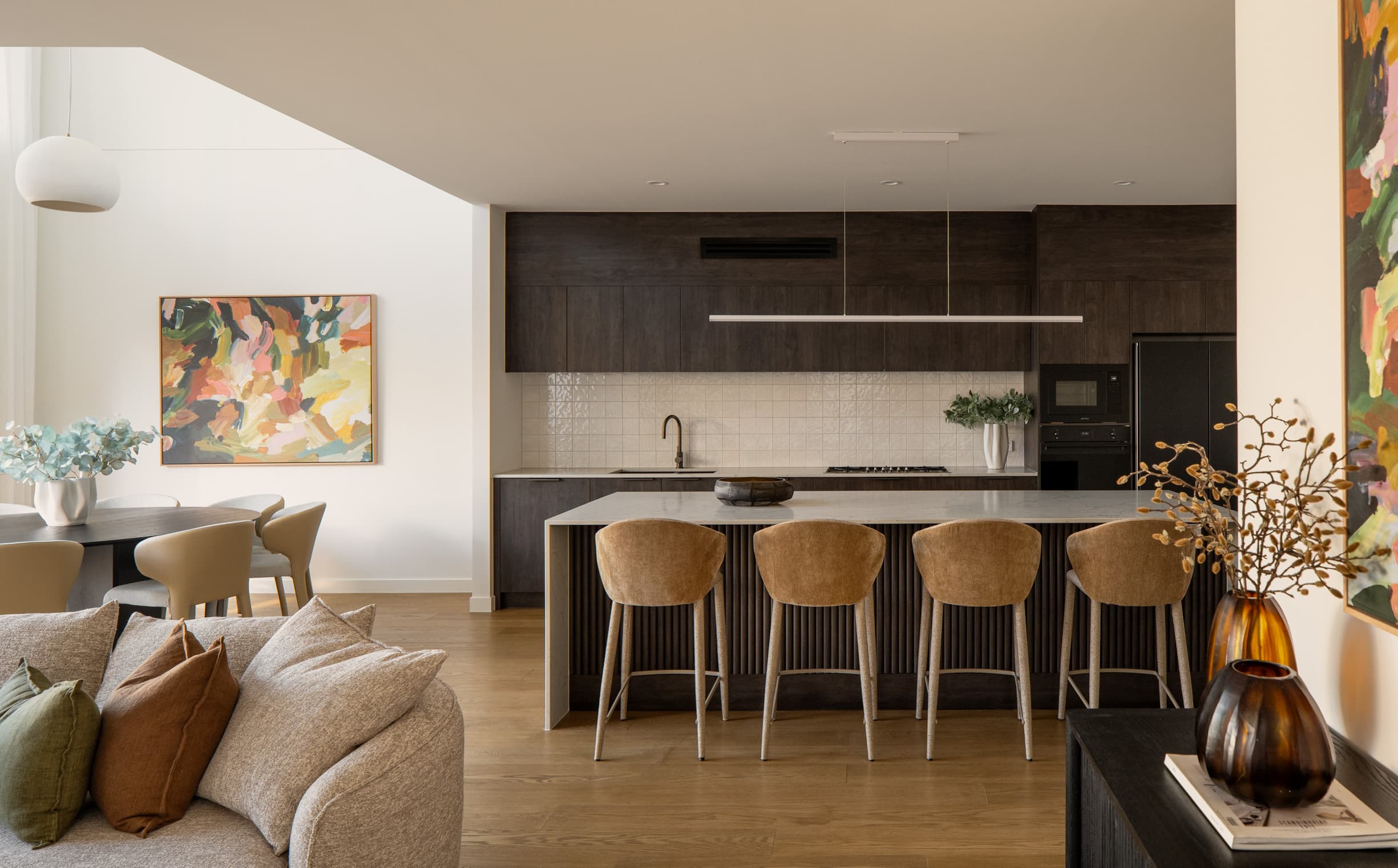 Lindsay House kitchen with dark timber joinery, a stone island and tan upholstered stools