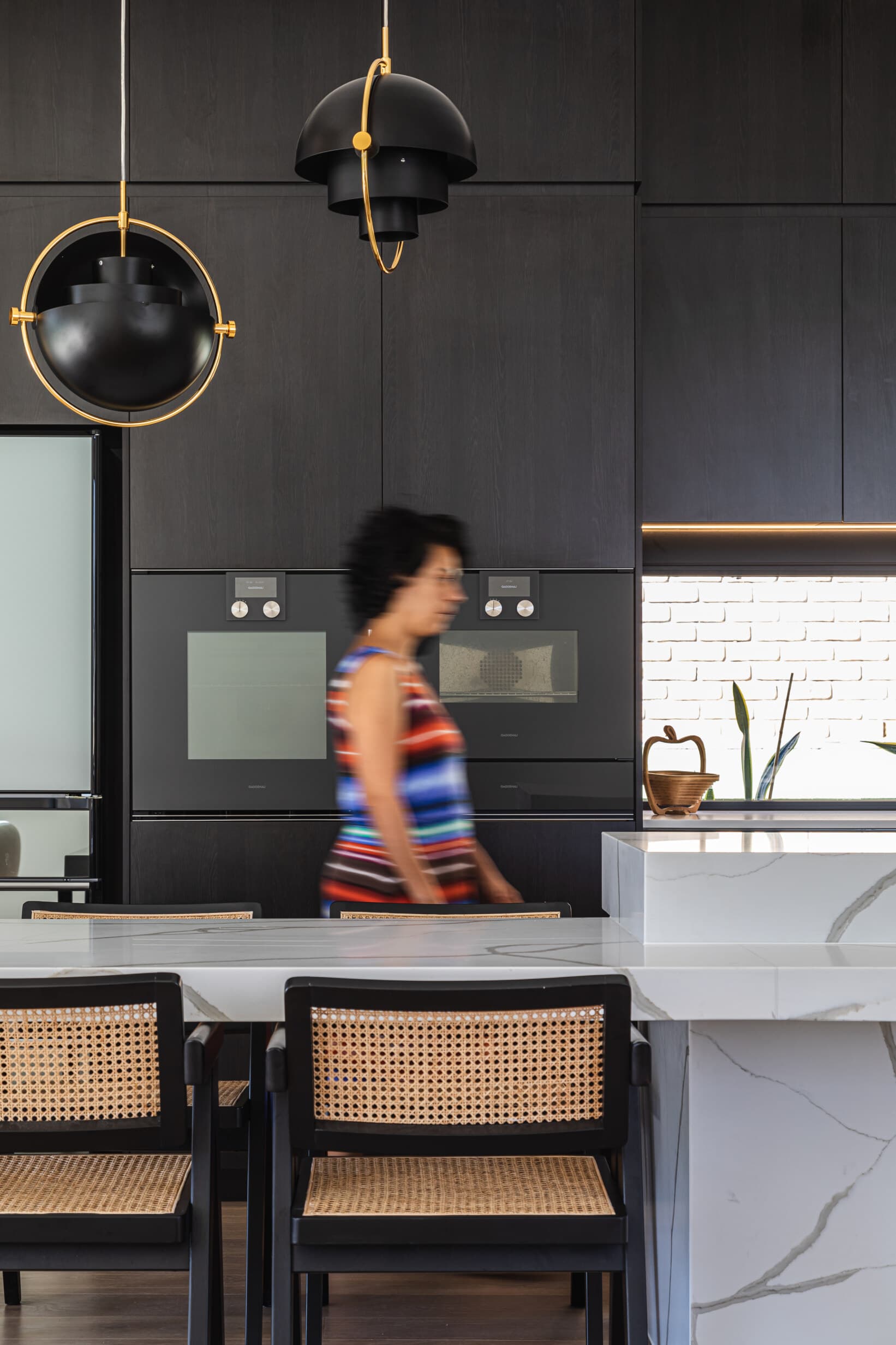 Z House kitchen island and black cabinetry under brass pendants
